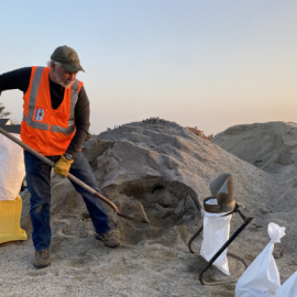 Volunteer wearing an orange safety vest scooping up sand into a sandbag
