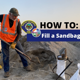 Man filling sandbag with shovel and dirt in orange vest